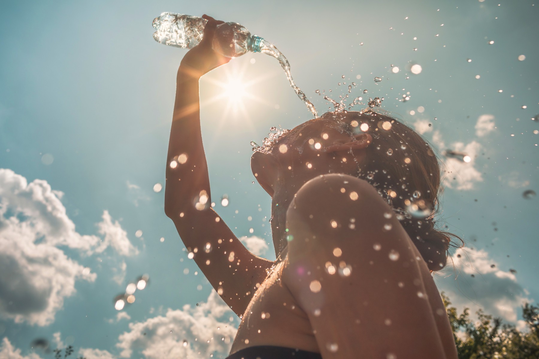 Frau giesst sich im Sonnenschein Wasser über den Kopf