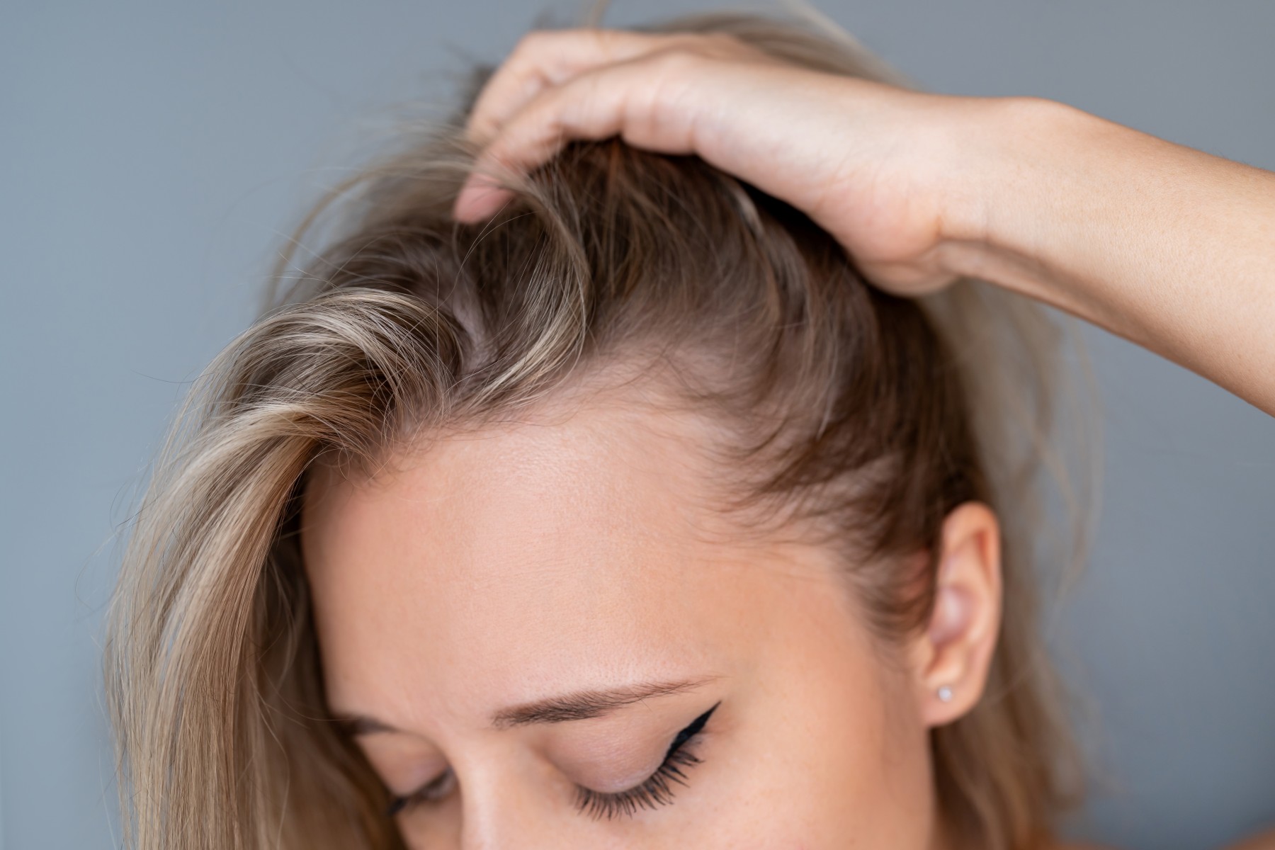 Frau mit langen blonden Haaren kratzt sich am Kopf