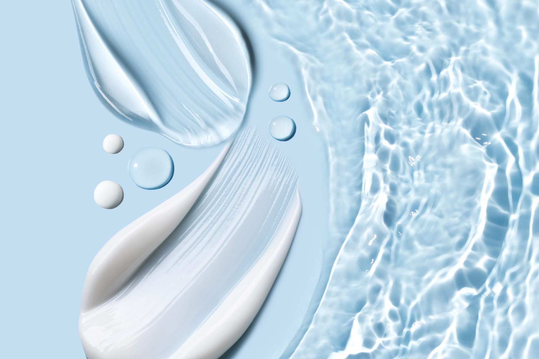Eine helle Creme liegt auf einem hellblauem Hintergrund und es sind einzelne Wassertropfen auf dem Untergrund zu sehen