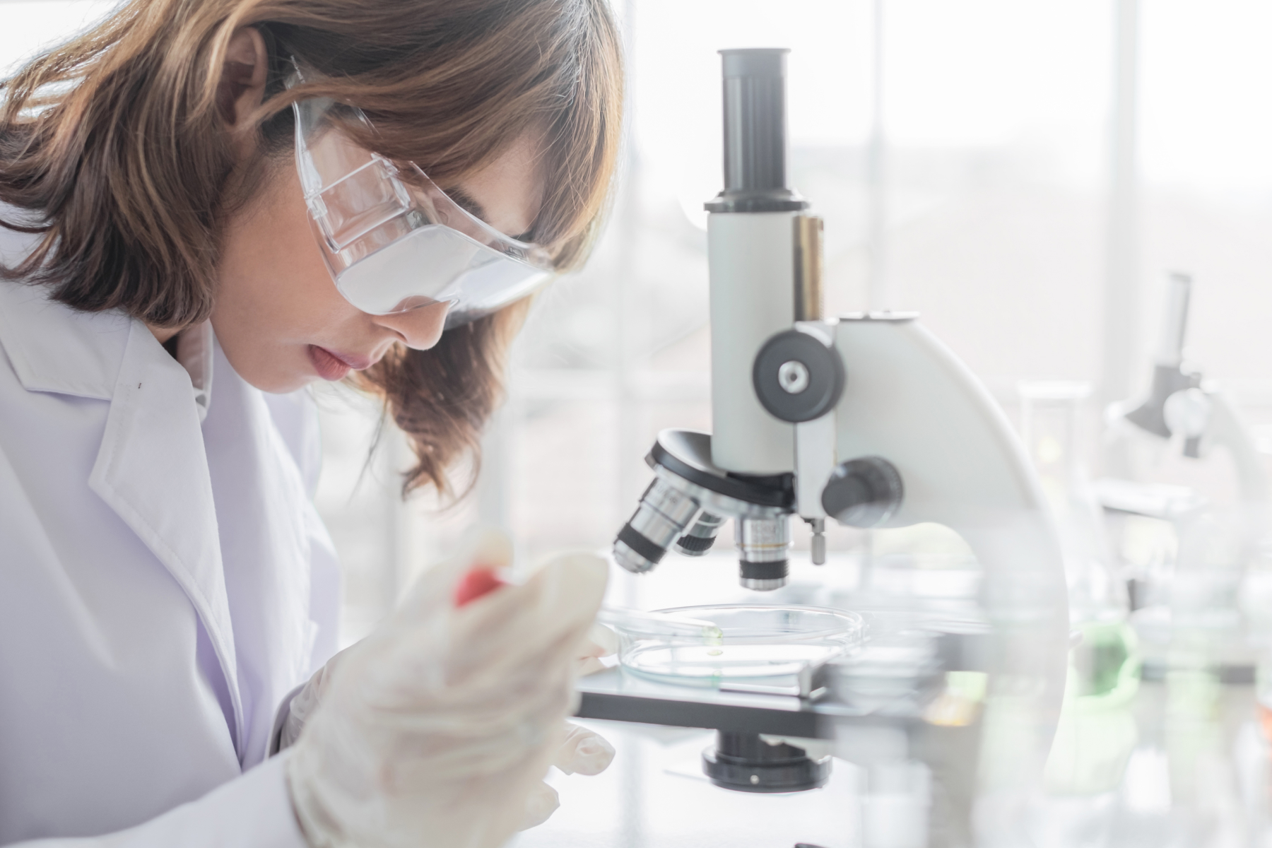 Eine Wissenschaftlerin mit weissem Kittel schaut durch ein Mikroskop
