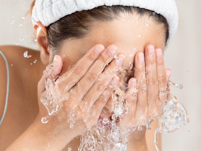 Frau wirft sich Wasser ins Gesicht über einem Lavabo