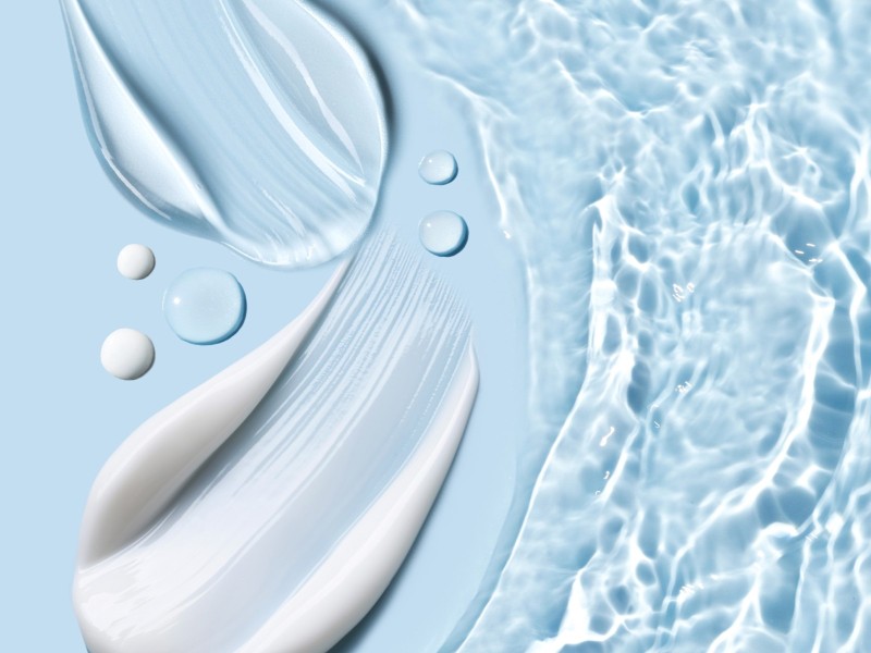 Helle Creme liegt auf einem hellblauen Hintergrund und es sind einzelne Wassertropfen zu sehen