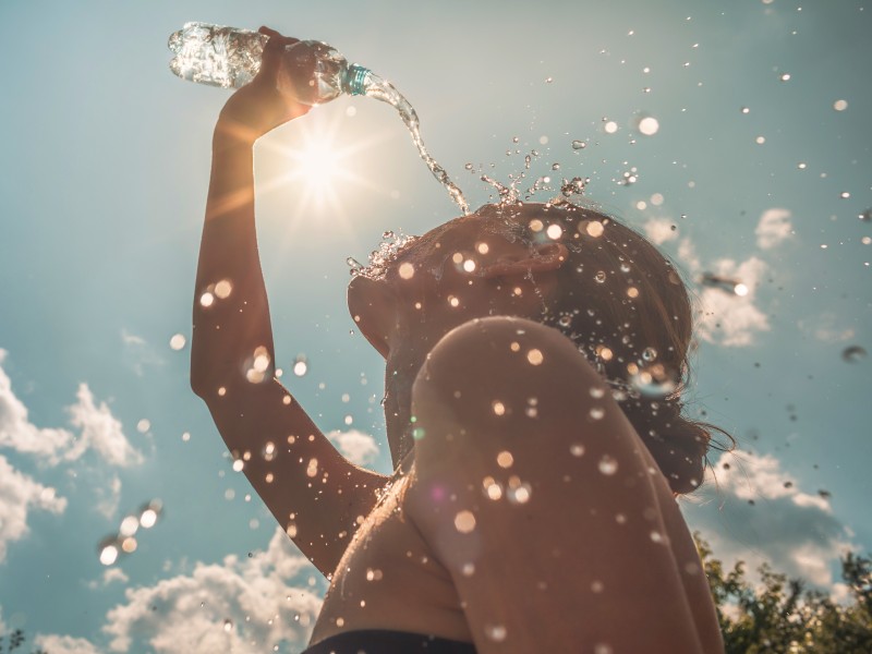 Frau giesst sich im Sonnenschein Wasser über den Kopf