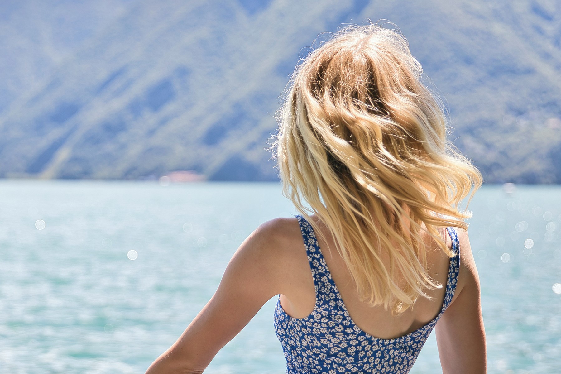 Frau steht mit dem Rücken zur Kamera vor dem Meer und trägt ihre Haare offen
