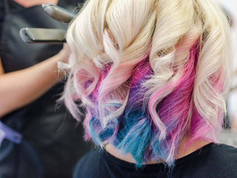Frau bei einer Hairstylistin. Die Frau hat weisse Haare mit verschieden farbigen Locken.